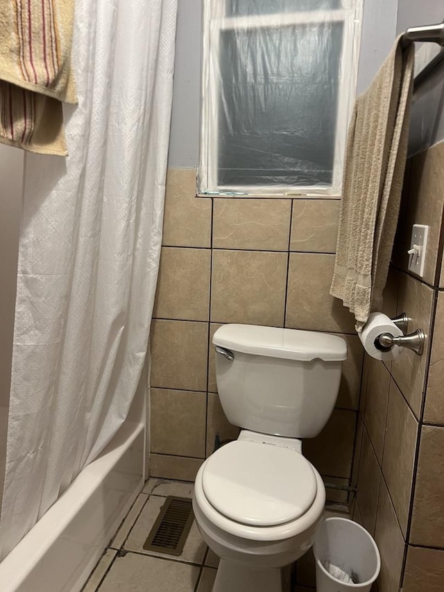 bathroom featuring shower / bath combo with shower curtain, toilet, tile patterned flooring, and tile walls