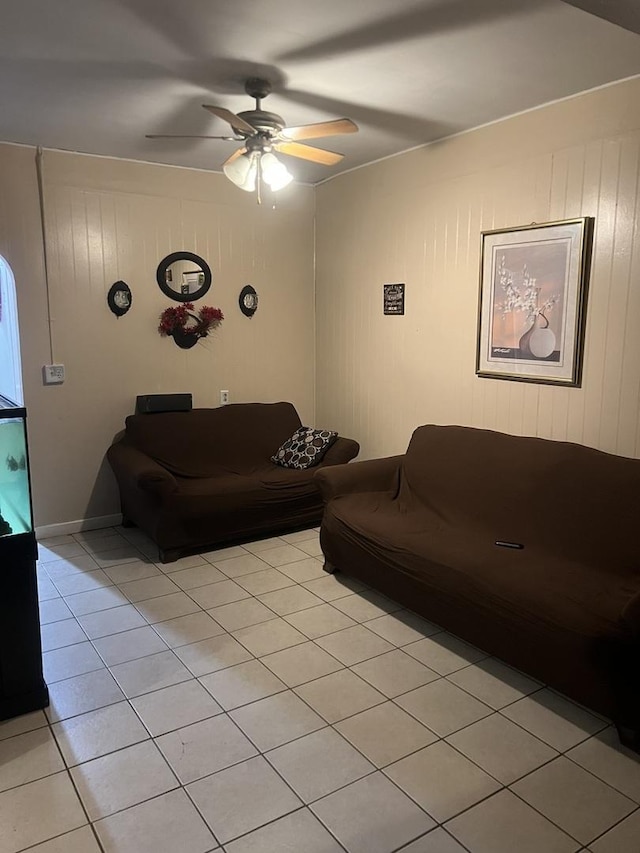 living room with ceiling fan, wood walls, and light tile patterned floors