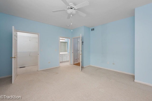 unfurnished bedroom with a walk in closet, light colored carpet, ceiling fan, and a closet