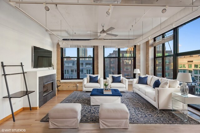 unfurnished living room with brick wall, plenty of natural light, ceiling fan, and light wood-type flooring