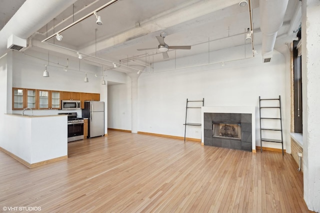 unfurnished living room with track lighting, a tile fireplace, ceiling fan, light hardwood / wood-style floors, and a high ceiling