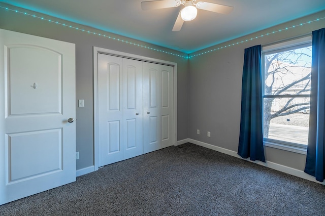 unfurnished bedroom with dark colored carpet, ceiling fan, and a closet