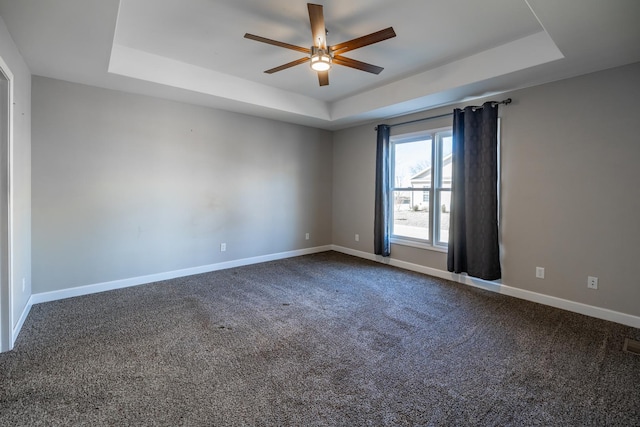 empty room with a raised ceiling, ceiling fan, and carpet flooring