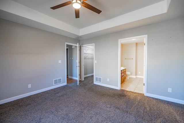 unfurnished bedroom featuring a walk in closet, light colored carpet, ceiling fan, ensuite bath, and a closet