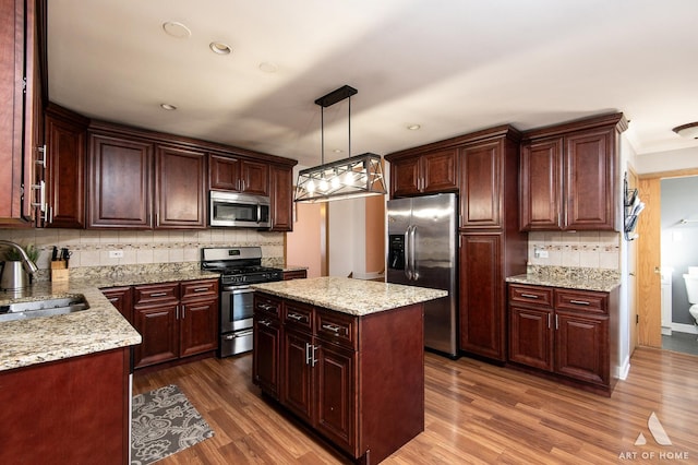 kitchen with a kitchen island, sink, hanging light fixtures, stainless steel appliances, and dark wood-type flooring