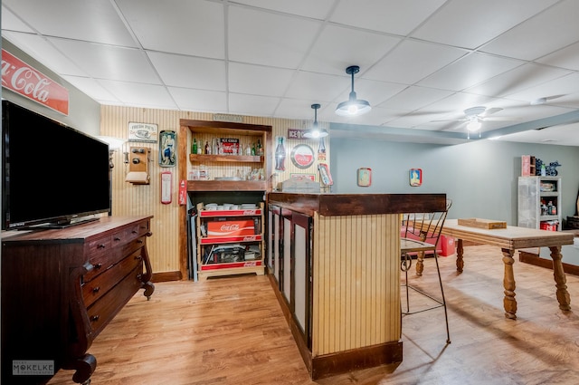 bar with ceiling fan, decorative light fixtures, a drop ceiling, and light wood-type flooring