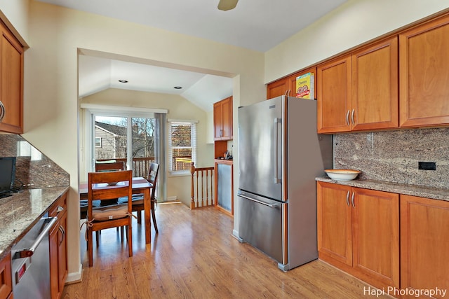 kitchen with vaulted ceiling, backsplash, light hardwood / wood-style floors, stainless steel appliances, and light stone countertops