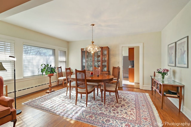 dining area with hardwood / wood-style flooring, a baseboard heating unit, and a chandelier