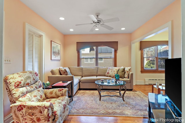 living room featuring a baseboard heating unit, a wealth of natural light, ceiling fan, and light hardwood / wood-style flooring