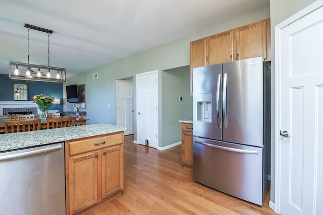 kitchen featuring pendant lighting, light wood-type flooring, light stone countertops, and appliances with stainless steel finishes