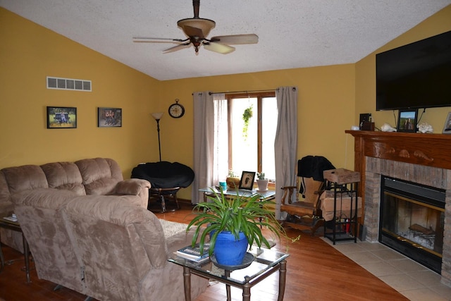 living room with lofted ceiling, ceiling fan, a tile fireplace, and a textured ceiling