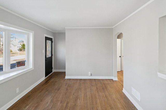 unfurnished room with arched walkways, baseboards, visible vents, and wood finished floors