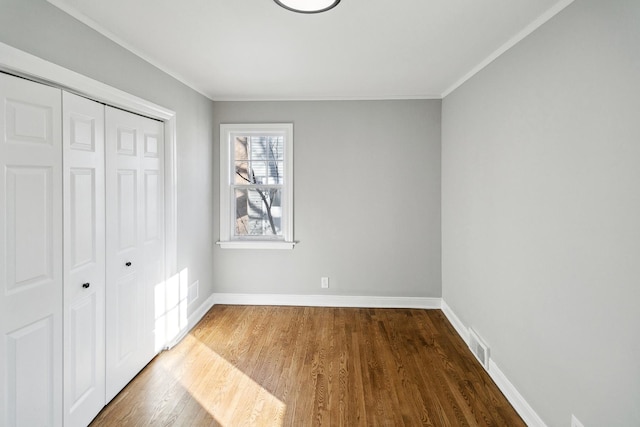 unfurnished bedroom with a closet, baseboards, crown molding, and wood finished floors