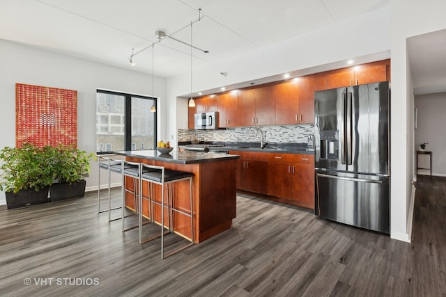 kitchen with pendant lighting, appliances with stainless steel finishes, a center island, a kitchen bar, and dark hardwood / wood-style flooring