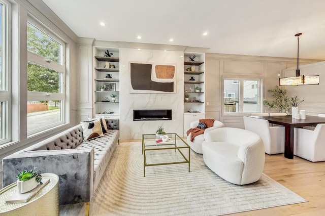 living room with built in features, a high end fireplace, and light hardwood / wood-style flooring