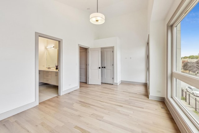 unfurnished bedroom featuring connected bathroom, light hardwood / wood-style floors, and a high ceiling