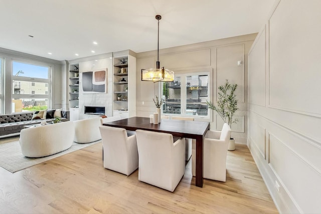 dining room featuring light wood-type flooring, a fireplace, and built in shelves