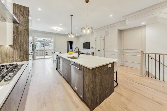 kitchen featuring sink, dark brown cabinets, stainless steel appliances, an island with sink, and wall chimney exhaust hood