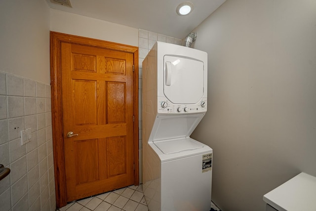 laundry room with stacked washing maching and dryer, tile walls, and light tile patterned floors