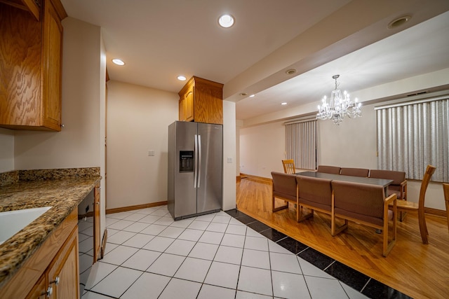 kitchen with light tile patterned flooring, black dishwasher, dark stone counters, a notable chandelier, and stainless steel refrigerator with ice dispenser