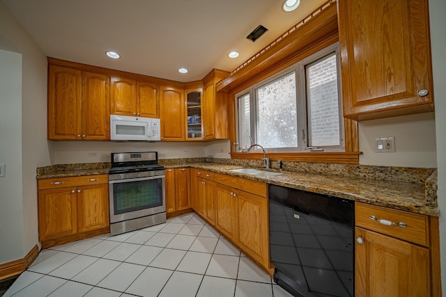 kitchen featuring dishwashing machine, sink, light tile patterned floors, stainless steel gas range oven, and light stone countertops