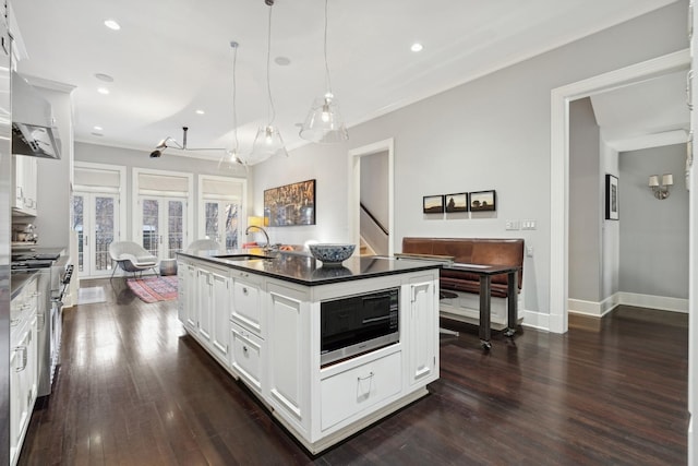 kitchen with built in microwave, high end range, a center island with sink, pendant lighting, and white cabinets