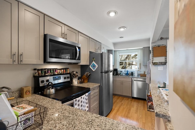 kitchen with appliances with stainless steel finishes, light stone countertops, light hardwood / wood-style floors, and gray cabinetry