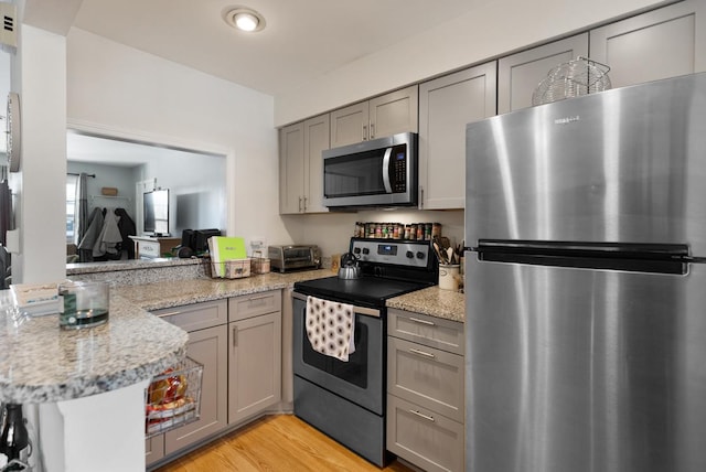 kitchen with light stone countertops, stainless steel appliances, kitchen peninsula, and light wood-type flooring