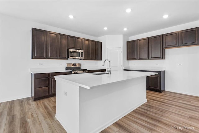 kitchen featuring stove, sink, a kitchen island with sink, and dark brown cabinets