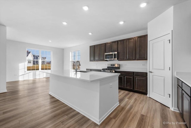 kitchen with sink, a kitchen island with sink, light hardwood / wood-style floors, stainless steel appliances, and dark brown cabinets