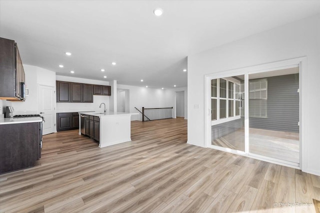 kitchen with sink, dark brown cabinets, light hardwood / wood-style flooring, and an island with sink