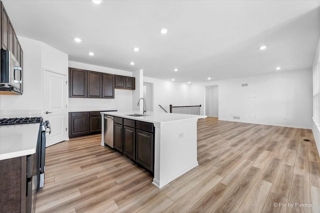 kitchen with sink, light hardwood / wood-style flooring, dark brown cabinets, stainless steel appliances, and a center island with sink