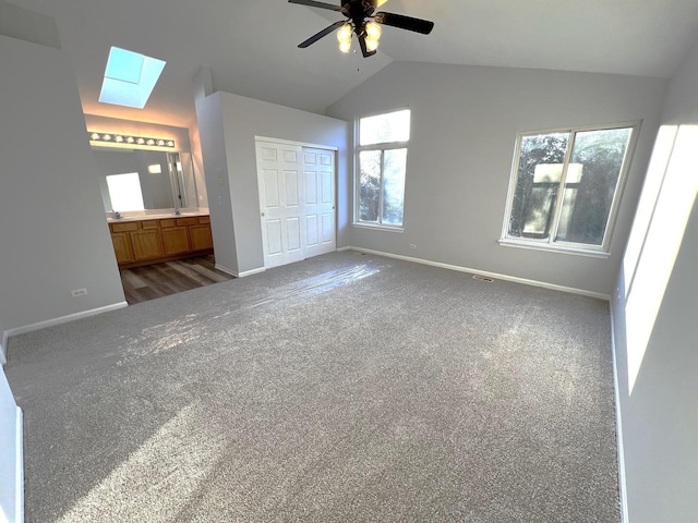 unfurnished bedroom featuring ensuite bathroom, lofted ceiling with skylight, dark colored carpet, a closet, and ceiling fan