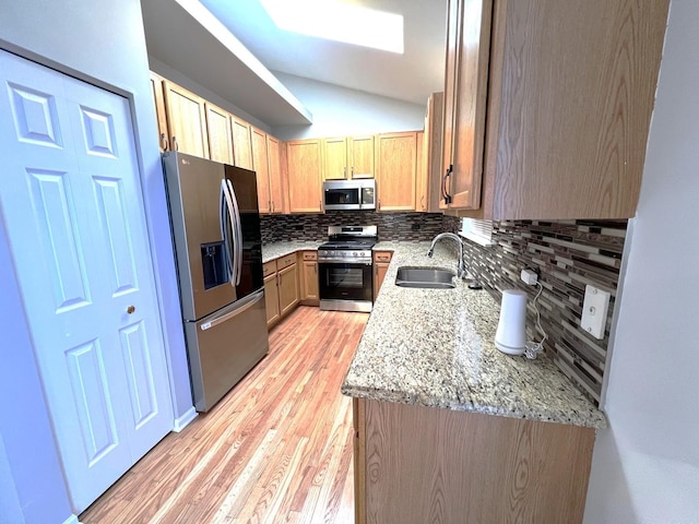 kitchen with lofted ceiling, sink, appliances with stainless steel finishes, tasteful backsplash, and light stone countertops