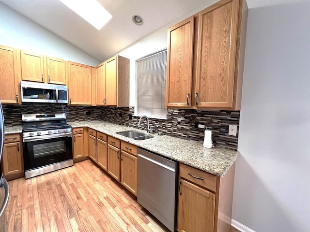 kitchen featuring lofted ceiling, sink, stainless steel appliances, light stone countertops, and light hardwood / wood-style flooring