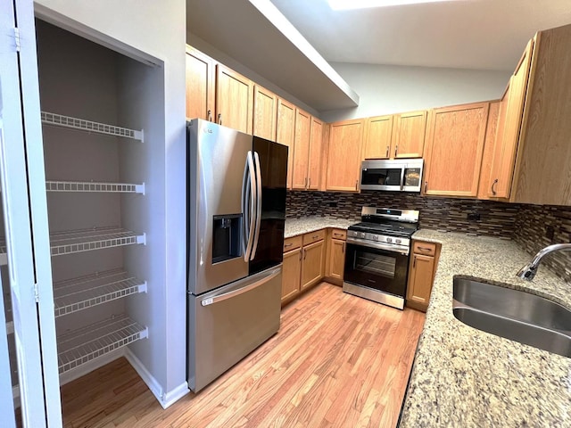 kitchen with sink, light stone counters, tasteful backsplash, vaulted ceiling, and stainless steel appliances