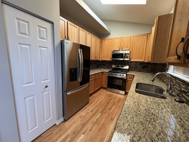 kitchen with lofted ceiling with skylight, sink, tasteful backsplash, appliances with stainless steel finishes, and light stone countertops