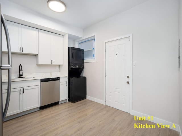 kitchen with sink, light hardwood / wood-style flooring, appliances with stainless steel finishes, white cabinetry, and stacked washer / dryer