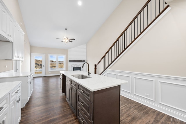 kitchen featuring a fireplace, white cabinetry, an island with sink, sink, and dark brown cabinets