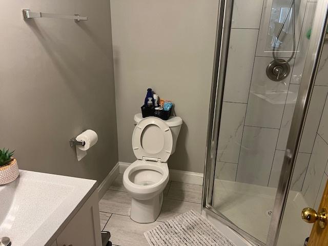 bathroom featuring tile patterned flooring, vanity, a shower with shower door, and toilet