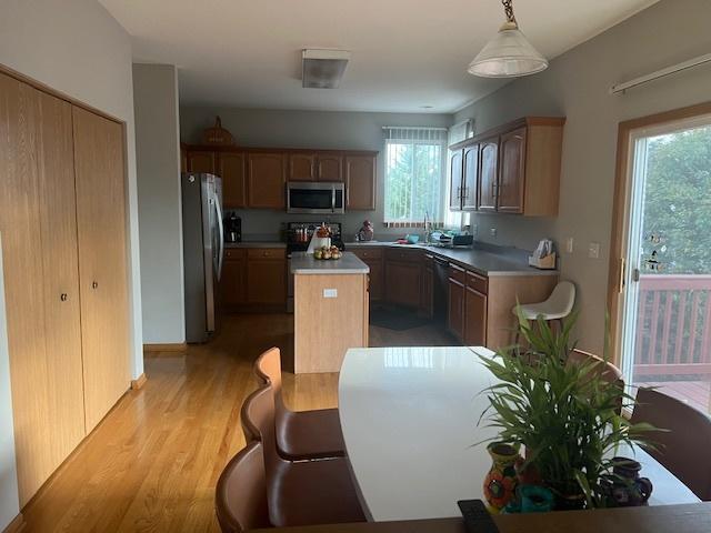 kitchen featuring light wood-type flooring, decorative light fixtures, a kitchen island, and appliances with stainless steel finishes