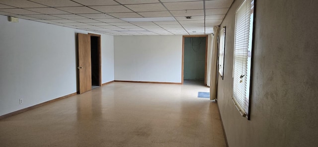 empty room with light floors, a drop ceiling, and baseboards