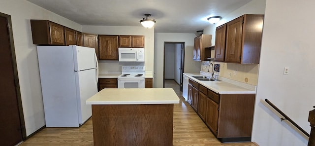 kitchen with white appliances, a sink, light countertops, a center island, and light wood finished floors