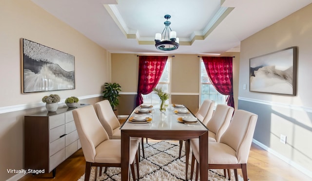 dining space with crown molding, a notable chandelier, a tray ceiling, and light hardwood / wood-style floors