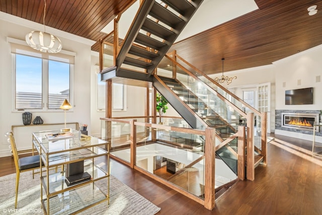 stairway with an inviting chandelier, ornamental molding, wood-type flooring, and wooden ceiling