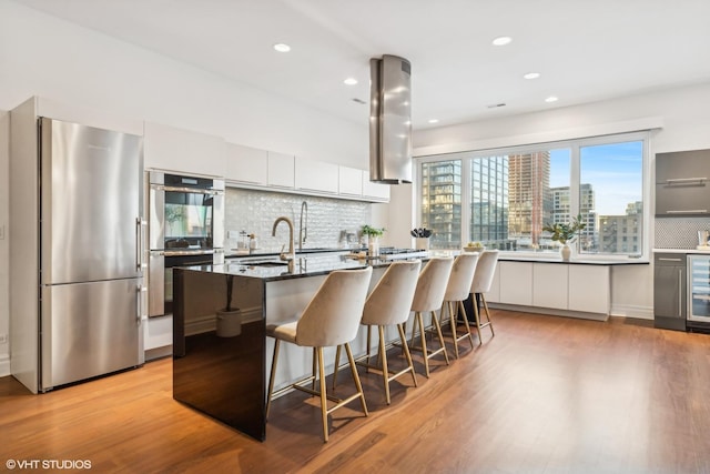 kitchen with stainless steel appliances, a kitchen breakfast bar, white cabinets, a center island with sink, and dark stone counters