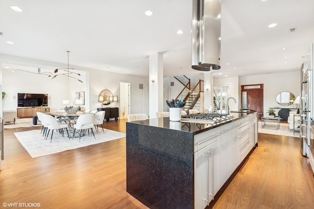 kitchen featuring decorative light fixtures, white cabinets, stainless steel gas cooktop, a center island with sink, and light hardwood / wood-style flooring