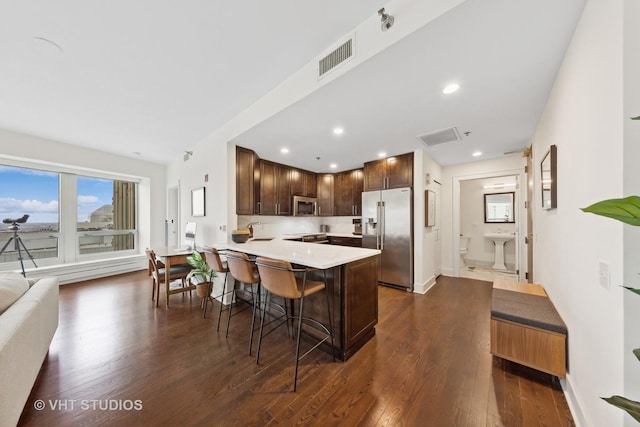 kitchen featuring dark wood-type flooring, a kitchen bar, sink, kitchen peninsula, and stainless steel appliances