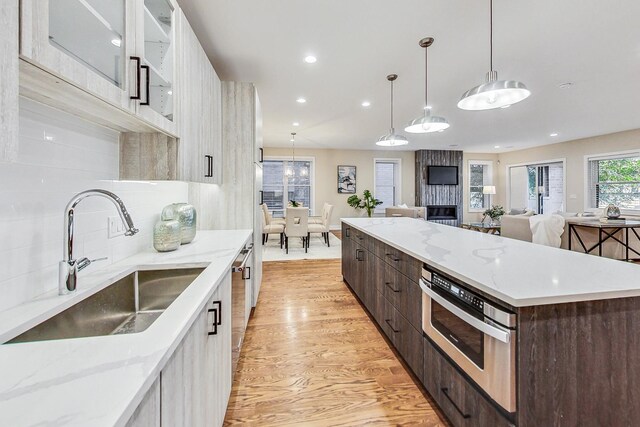 kitchen with pendant lighting, sink, dark brown cabinetry, decorative backsplash, and light wood-type flooring