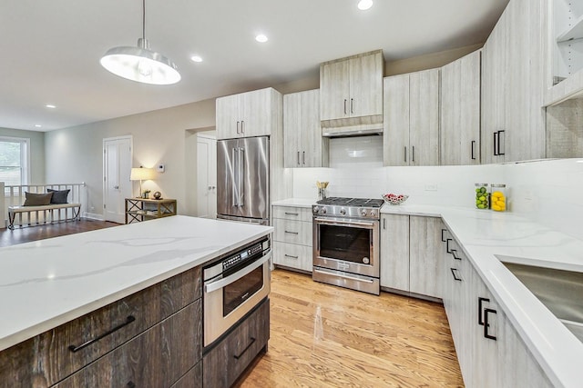 kitchen featuring backsplash, hanging light fixtures, high end appliances, light stone counters, and light hardwood / wood-style floors